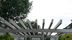 A covered walkway with a concrete path flanked by neatly trimmed bushes and a pergola structure. - Steps from watching Sunsets in the Sand (Carpinteria)