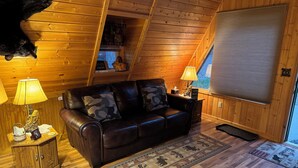 L’intérieur chaleureux d’un chalet avec un canapé en cuir, des murs en bois, un tapis et une tête d’animal empaillée accrochée au mur.
