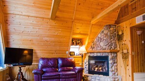 Un intérieur en bois avec une cheminée en pierre, un canapé en cuir et un téléviseur.