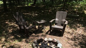 Un terrain de camping équipé de deux fauteuils Adirondack, d’une petite table et d’un foyer entouré de pierres.