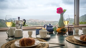 A table set with a croissant, a teapot, a vase with a flower, and glasses of wine, with a scenic view in the background. - Fantastic apartment with sea views in prime location (Santa Reparata di Balagne)