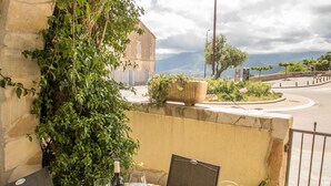A round table with a green and yellow patterned tablecloth, two chairs, a bottle of wine, and a glass. - Fantastic apartment with sea views in prime location (Santa Reparata di Balagne)