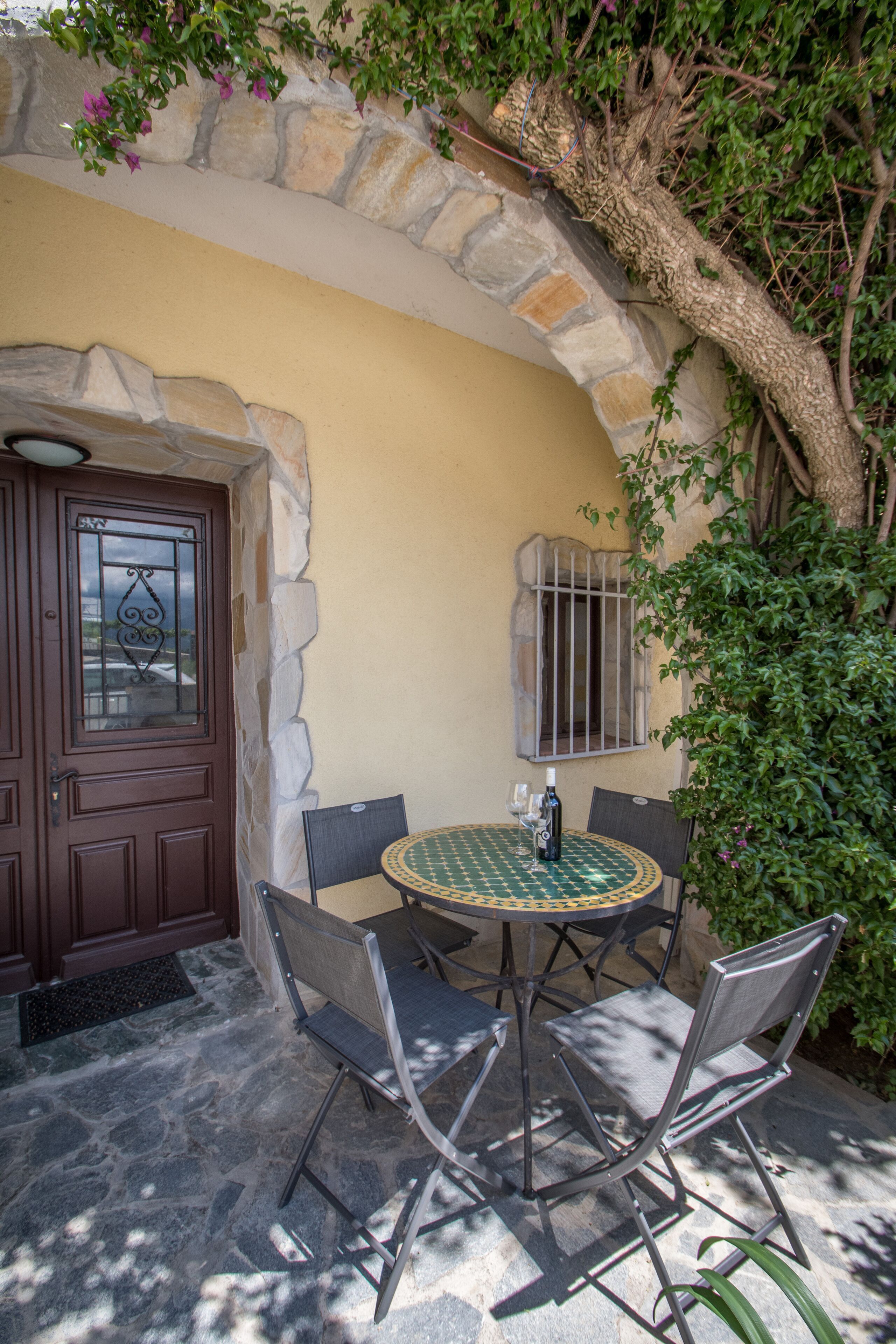 Une terrasse extérieure avec un mur en pierre, une porte en bois et une table avec des chaises.