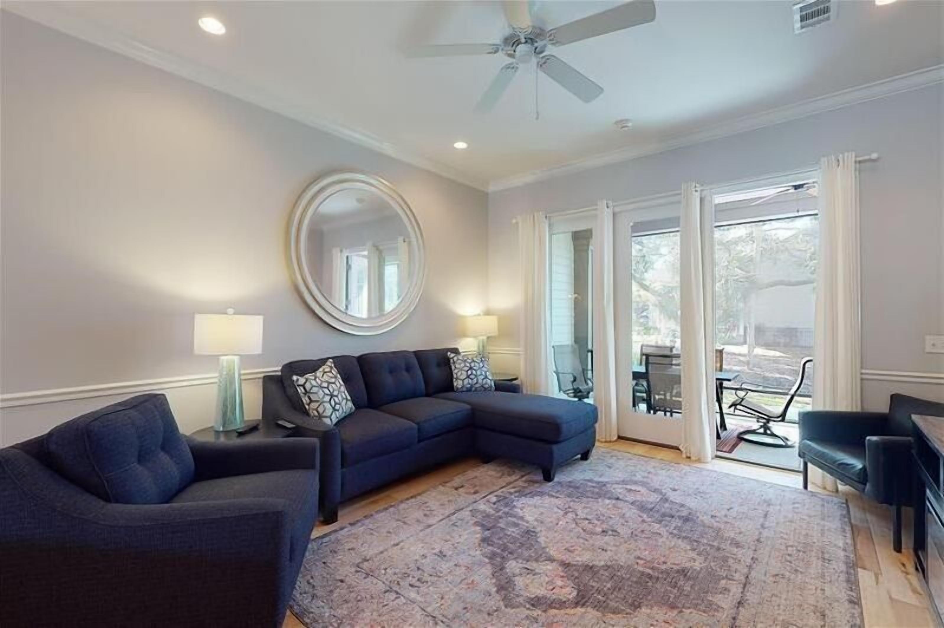 A living room with a sectional sofa, a round mirror, and a ceiling fan.