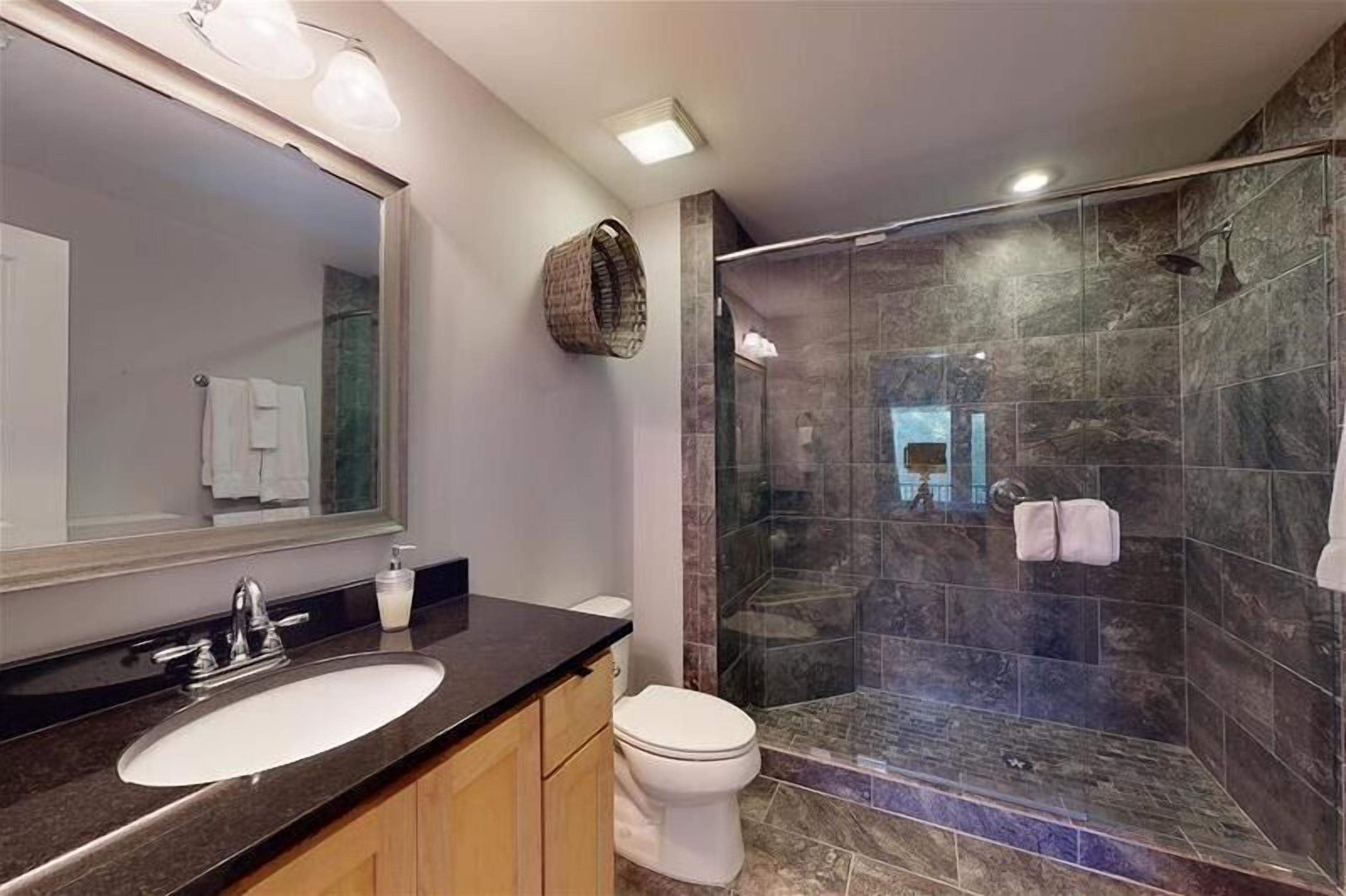 Un baño moderno con un espejo grande, un lavabo, un inodoro y una zona de ducha con mampara de vidrio.