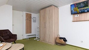 Et værelse med en brun læderstol, et lille rundt bord, en træskab og et fjernsyn ophængt på væggen, samt et grønt tæppe.
