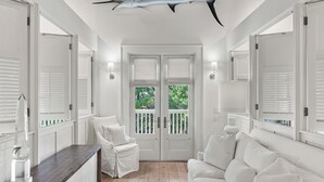 Een ruime kamer met een houten plafond, een plafondventilator, een witte bank, een witte fauteuil en een zacht vloerkleed.
