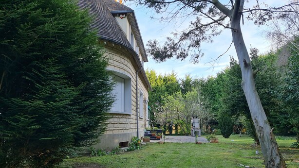 A house with a curved roof, surrounded by a well-maintained garden with various plants and a lawn. - Your holidays in a beautiful property (Varaville)