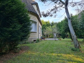 A house with a curved roof, surrounded by a well-maintained garden with various plants and a lawn.