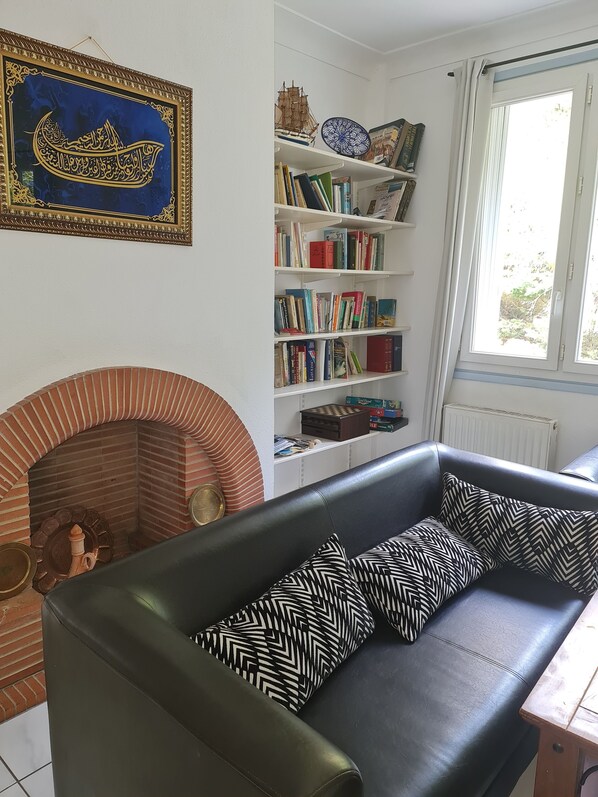 A living room with a fireplace, a sofa, a bookshelf, and a window.