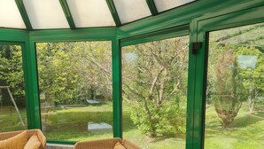 A conservatory with wicker furniture and a view of a garden. - Your holidays in a beautiful property (Varaville)