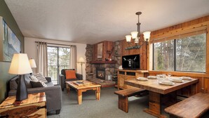A rustic interior with a stone fireplace, wooden furniture, and large windows offering a view of the outdoors. - Beaver Village Unit #1824 Updated 2 bed close to downtown & outdoor activities (Winter Park)