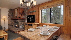 A wooden dining area with a stone fireplace, a television, and a large window with a forest view. - Beaver Village Unit #1824 Updated 2 bed close to downtown & outdoor activities (Winter Park)