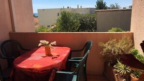 Ein kleiner Balkon mit Tisch und Stühlen, einer Blumenvase und Topfpflanzen.