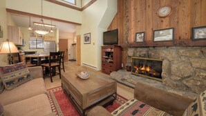 A spacious living room with a fireplace, wooden walls, and a dining area with a high ceiling.