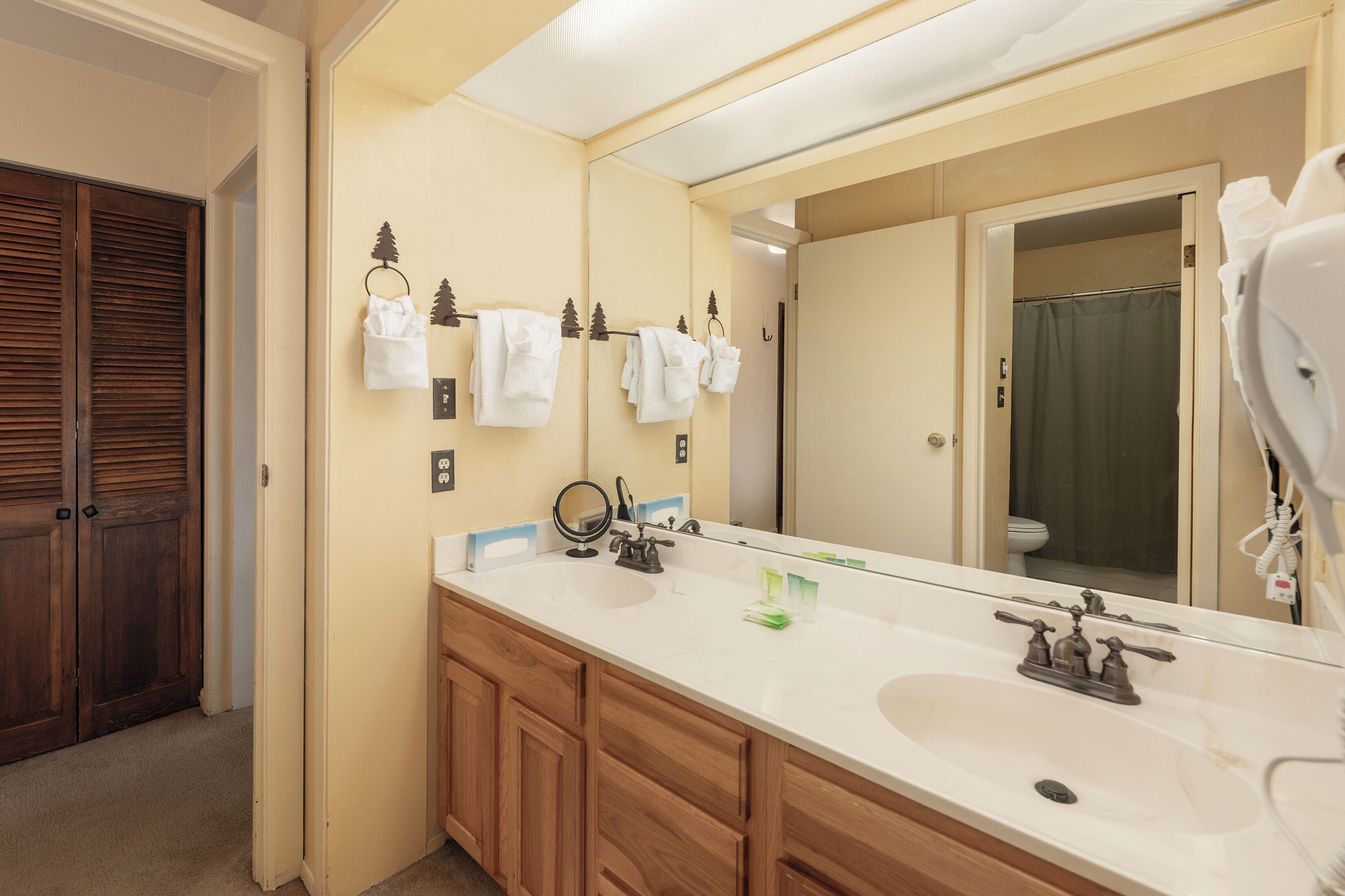 A bathroom with two sinks, wooden cabinets, a large mirror, and a shower area.