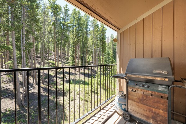 A balcony with a grill and a view of a forest.