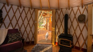 Un intérieur de tente chaleureux avec un plancher en bois, un canapé, une cheminée et une vue sur une terrasse extérieure en bois.