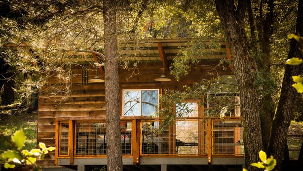 Une cabane en bois dotée d’un balcon, entourée d’arbres.