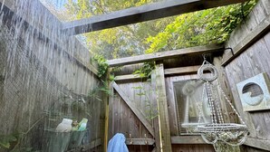 Ein rustikales Badezimmer aus Holz mit Regendusche, einer hängenden Makramee-Dekoration und einem Handtuch an der Wand.