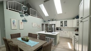 Eine moderne Küche mit weißen Schränken, einer zentralen Kochinsel und einem Essbereich mit Korbstühlen und einem Holztisch.