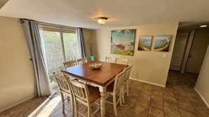 A dining area with a wooden table and white chairs, a window with curtains, and a painting on the wall. - Spacious, Updated Villa – Perfect for Family Beach Vacations, Two King Beds! (Hilton Head Island)