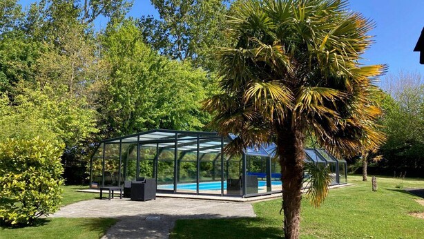 A glass-enclosed structure with a pool, surrounded by lush greenery and a palm tree.