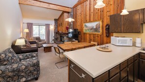Una sala acogedora con chimenea, paredes de madera, una mesa de comedor y una cocina con microondas.