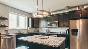 A modern kitchen with dark cabinets, stainless steel appliances, a granite countertop island, and a built-in oven. - Spacious Cowboy home near East Nashville with rooftop and views (Nashville)