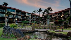 A hotel with multiple-story buildings, a central courtyard with a small pond, and surrounding palm trees. - Luxury oceanfront studio with spacious lanai (Lahaina)