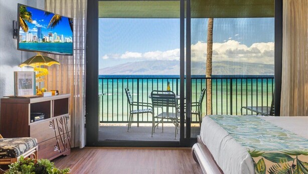A hotel room with a large balcony, a television, a desk with chairs, and a bed. - Luxury oceanfront studio with spacious lanai (Lahaina)