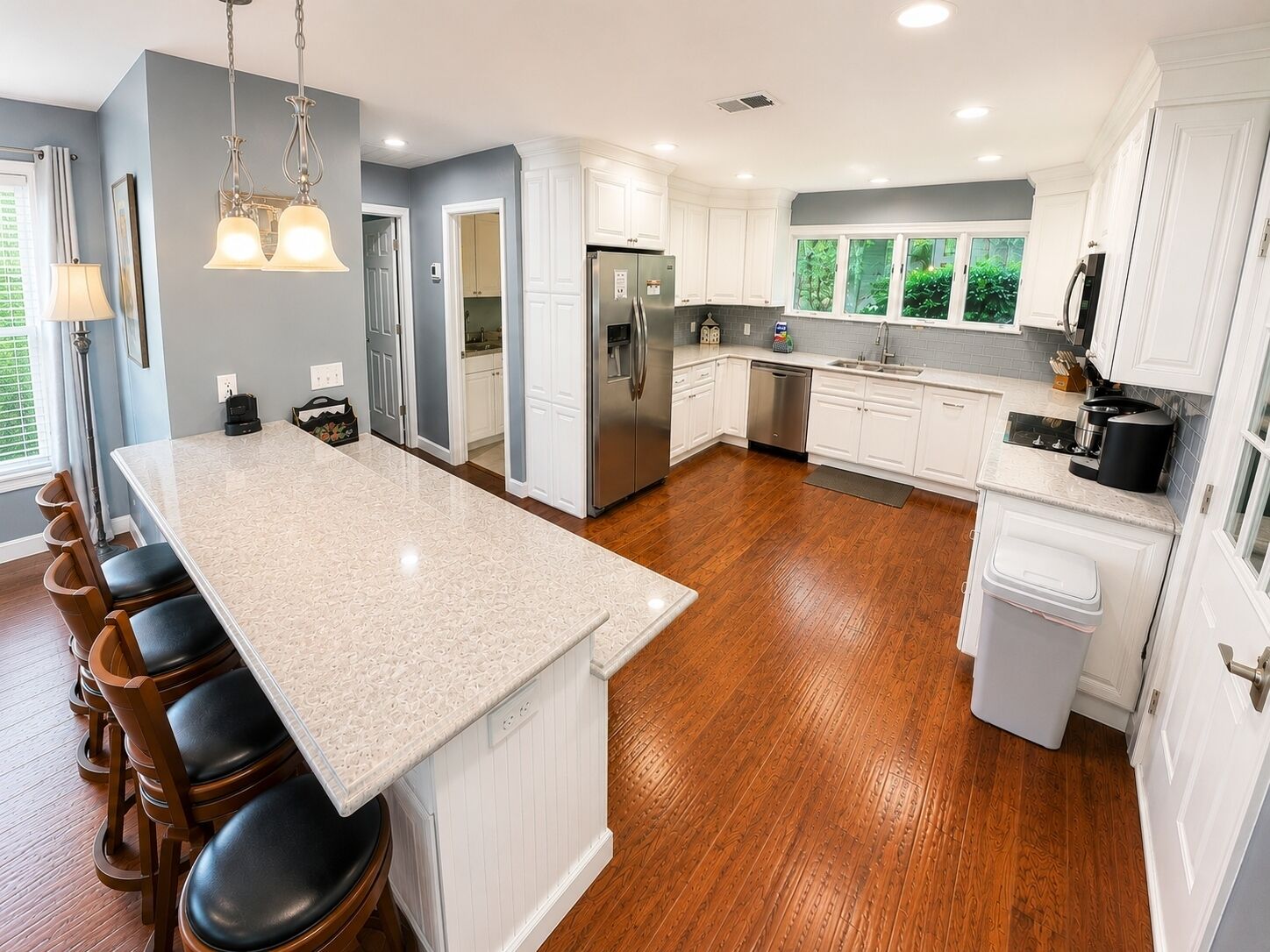 A modern kitchen with a central island, stainless steel appliances, and a view of greenery outside.