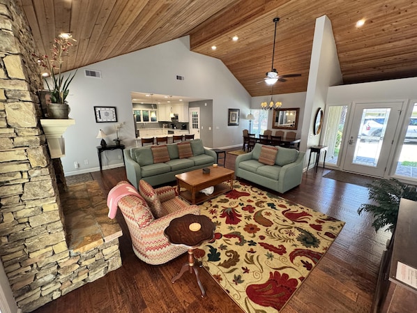 A spacious living area with a stone wall, wooden ceiling, and a view into the kitchen.