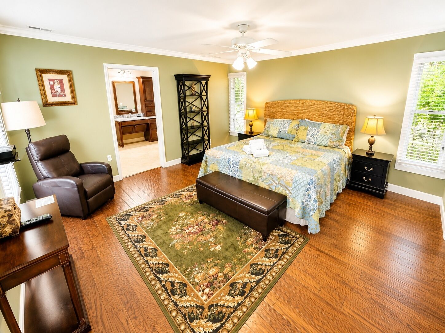 A bedroom with a bed, a chair, a nightstand, a lamp, a bench, a rug, and a ceiling fan.
