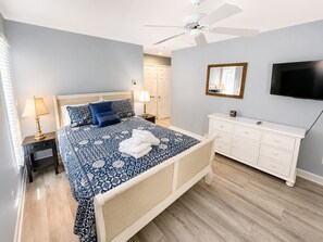 A bedroom with a bed, bedside tables, a dresser, a ceiling fan, a television, and a mirror.