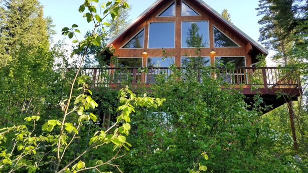 Una baita di legno con ampie finestre e un balcone, immersa in una fitta foresta.