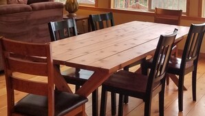Zona pranzo con tavolo e sedie in legno, ampie finestre con vista sugli alberi e lampadario a sospensione.