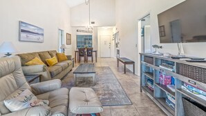 A spacious living room with a leather sofa, a coffee table, and a bookshelf filled with books. - Updated & Open, Sea Woods Veranda. Walking Distance to Beach - SV227 (New Smyrna Beach)