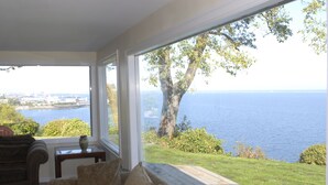 A room with a large window overlooking a body of water and a grassy area. -  Best View in Port Angeles: The Bluff House  (Port Angeles)
