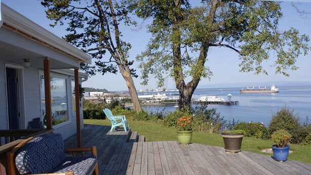 A wooden deck with a sofa and chairs, a potted plant, and a view of the sea and ships. -  Best View in Port Angeles: The Bluff House  (Port Angeles)