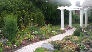 A garden with a brick pathway, various plants, and a pergola structure. -  Best View in Port Angeles: The Bluff House  (Port Angeles)