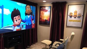 A home theater with a large flat-screen TV, comfortable seating, and movie posters on the wall. - Premium 5 Bedroom Home-Theatre, BBQ, GYM, Hot-Tub and Arcade (Spokane)