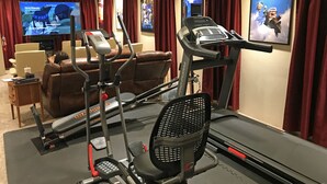 A home theater with a large screen, a treadmill, and a stationary bike. - Premium 5 Bedroom Home-Theatre, BBQ, GYM, Hot-Tub and Arcade (Spokane)