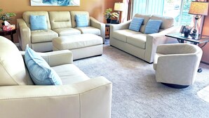 A living room with a beige sofa set, a glass coffee table, and a large abstract painting on the wall. - Premium 5 Bedroom Home-Theatre, BBQ, GYM, Hot-Tub and Arcade (Spokane)