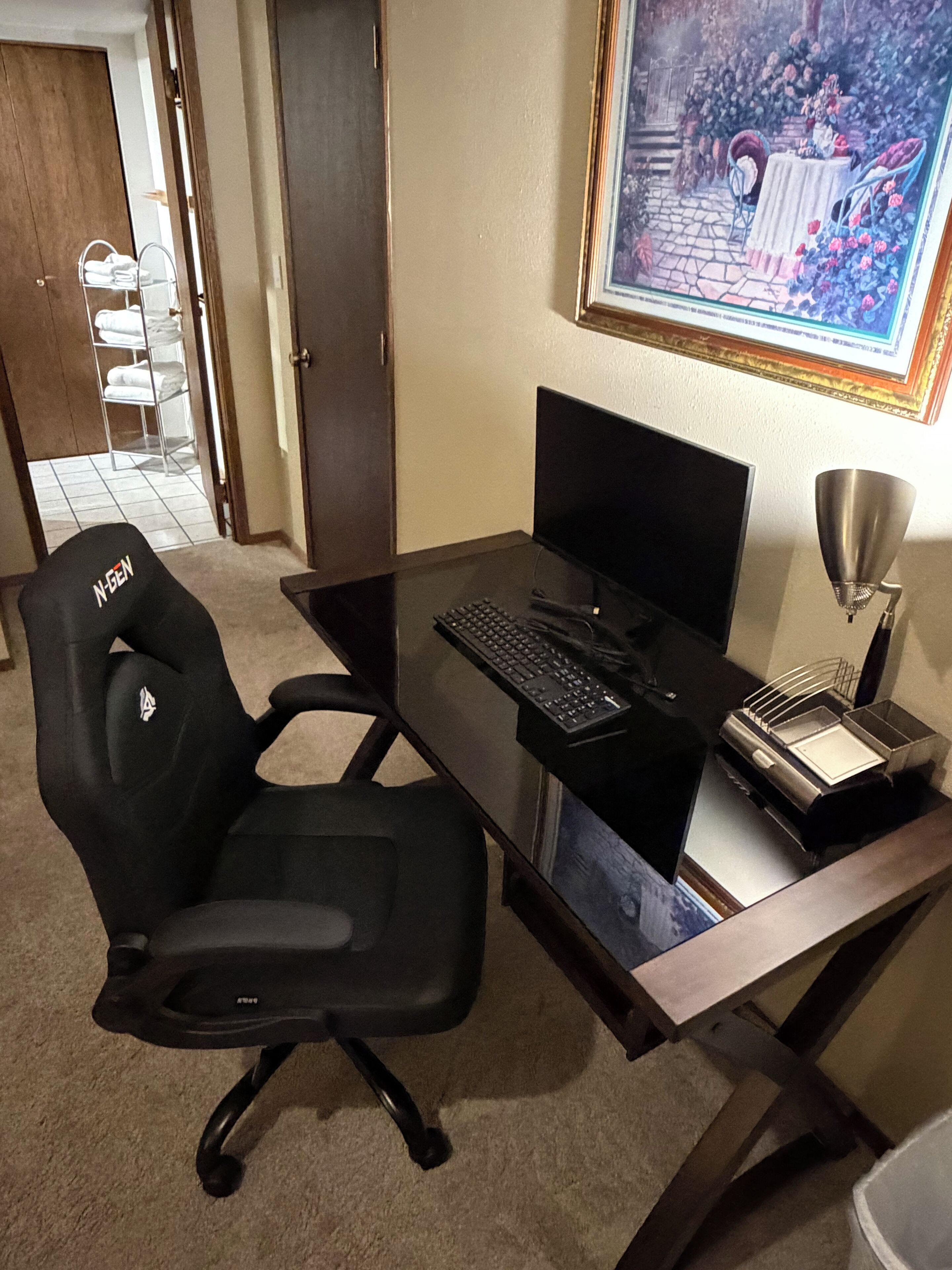 A home office setup with a desk, chair, computer, keyboard, and a lamp.