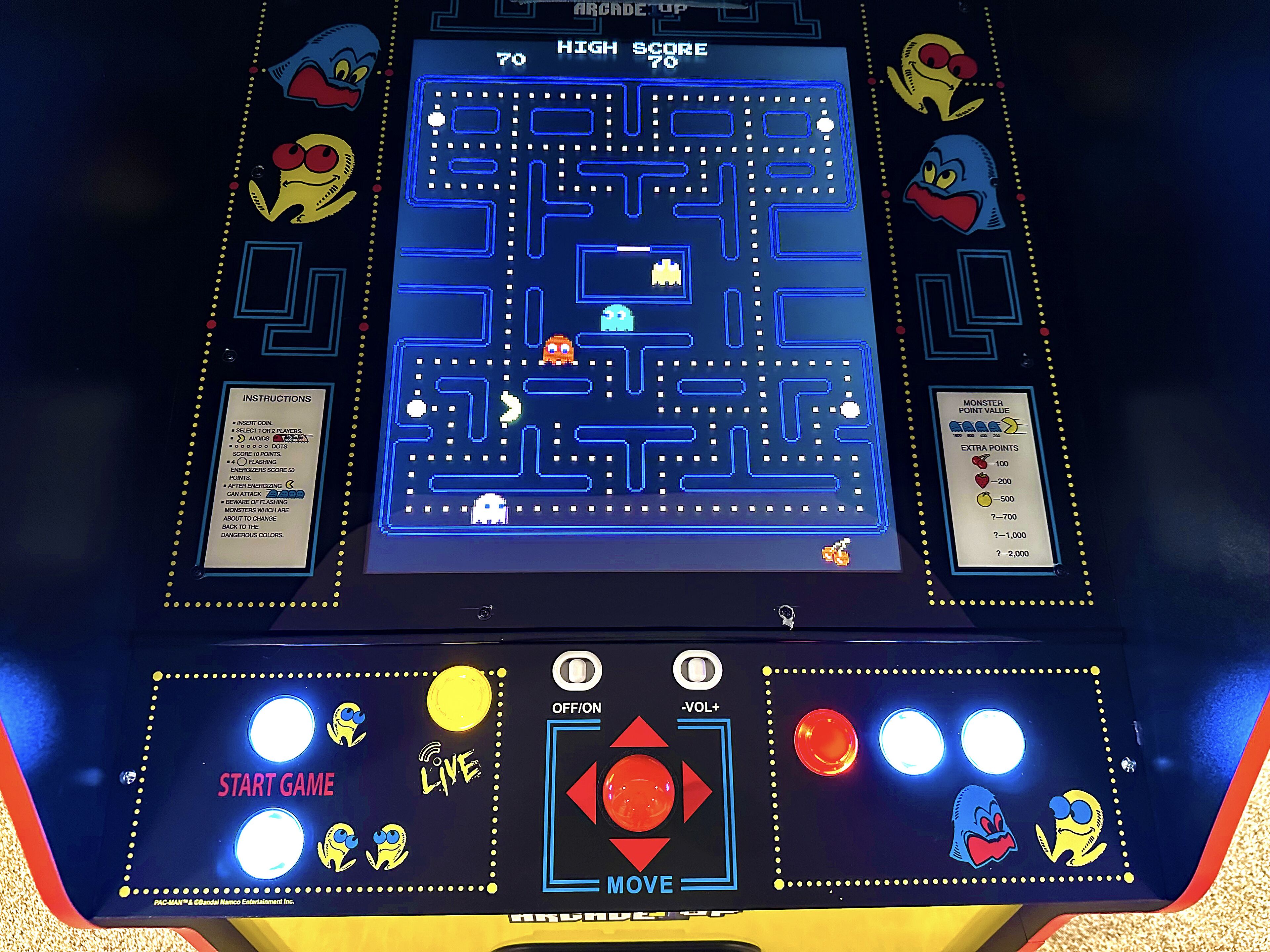 Jogo de arcade Pac-Man com labirinto, visor de pontuação e botões de controle.