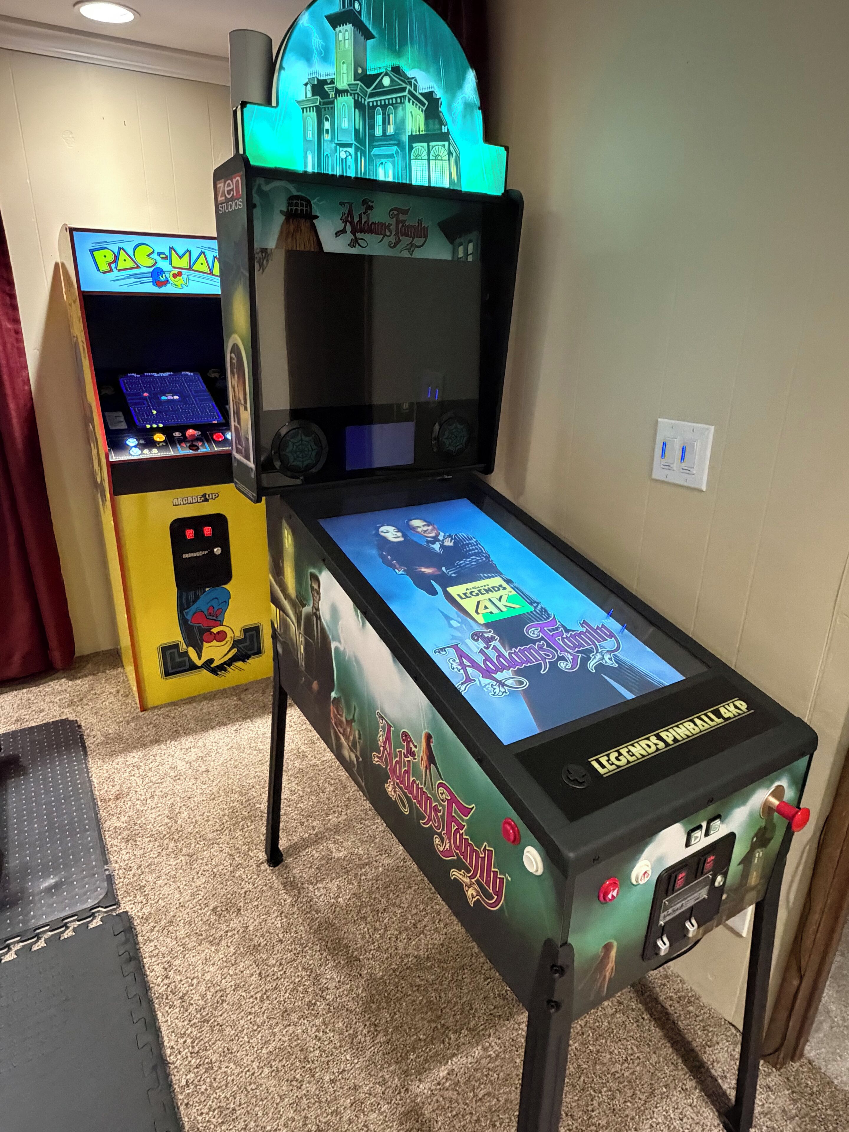 A pinball machine with 'Legends Pinball 4K' and 'Adams Family' themes, featuring a green-lit top section and a colorful playfield.