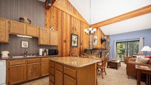 A kitchen with wooden cabinets, a granite countertop island, and a dining area with chairs. - Beaver Village Unit #1633 Classic 2 bed clean and comfortable with full kitchen (Winter Park)