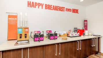 Una estación de desayuno con máquinas para hacer gofres, dispensadores de masa para gofres y un letrero que dice 'HAPPY BREAKFAST START HERE'.