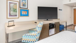 Een hotelkamer met een bed, een bureau met een flatscreen televisie, een magnetron en een stoel met een gestreept kussen.